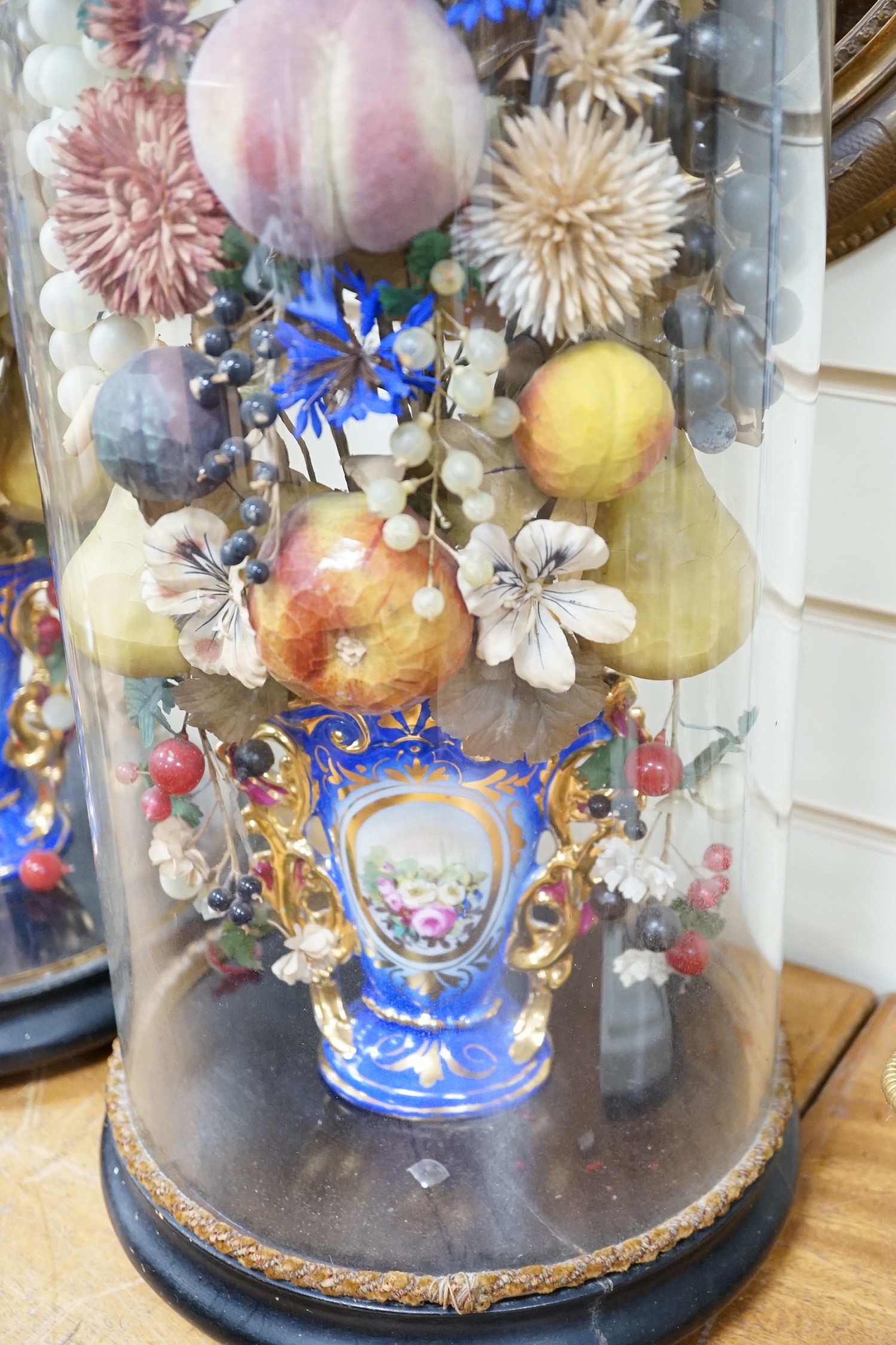 A pair of Victorian displays of painted papier mache fruit in vases, under glass domes, 58cms high